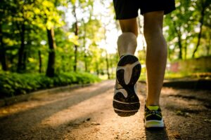 Close-up of a man's legs from behind as he is running on a trail in the woods. He is wearing sneakers.